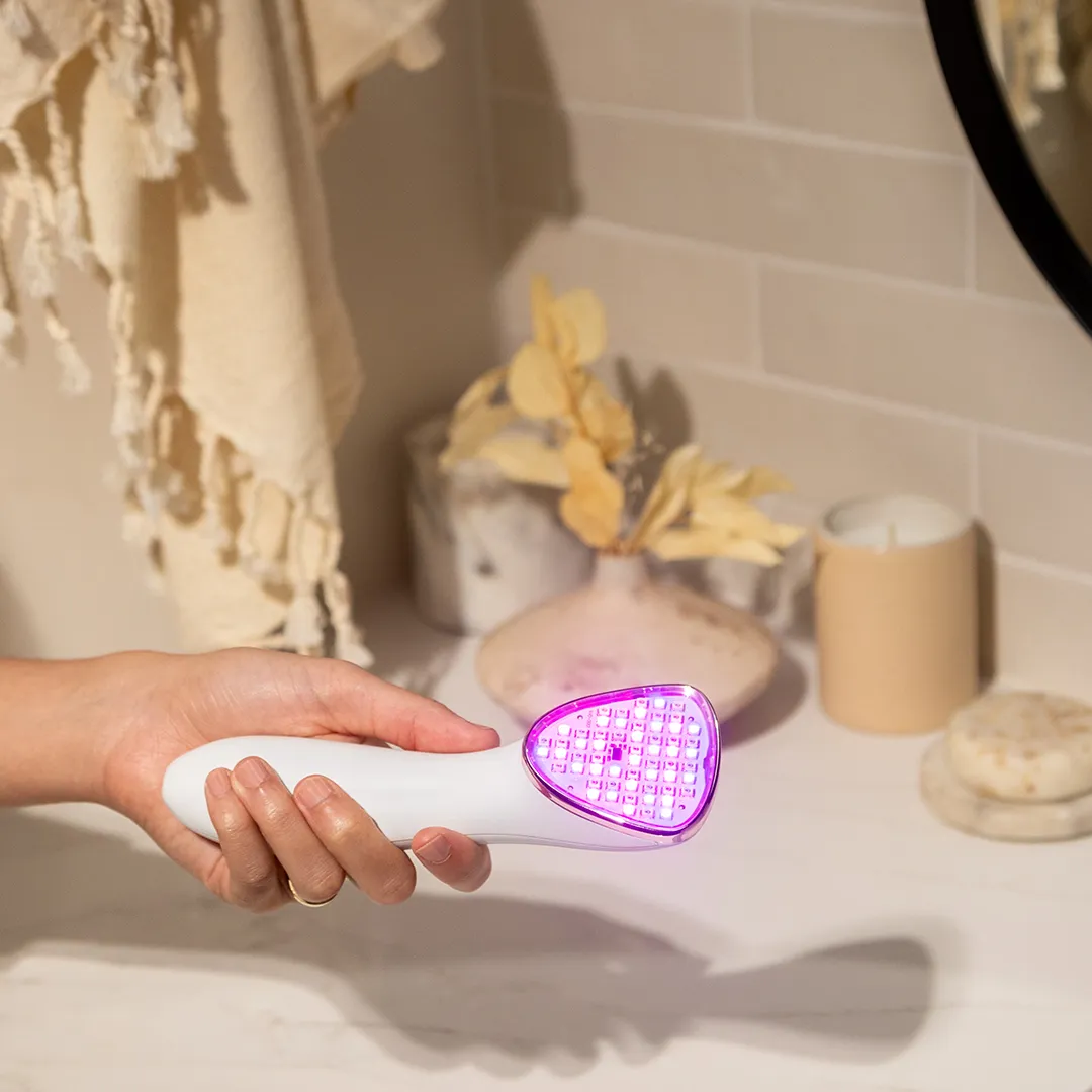 reVive Clinical light therapy device held beside a warm-toned bathroom counter